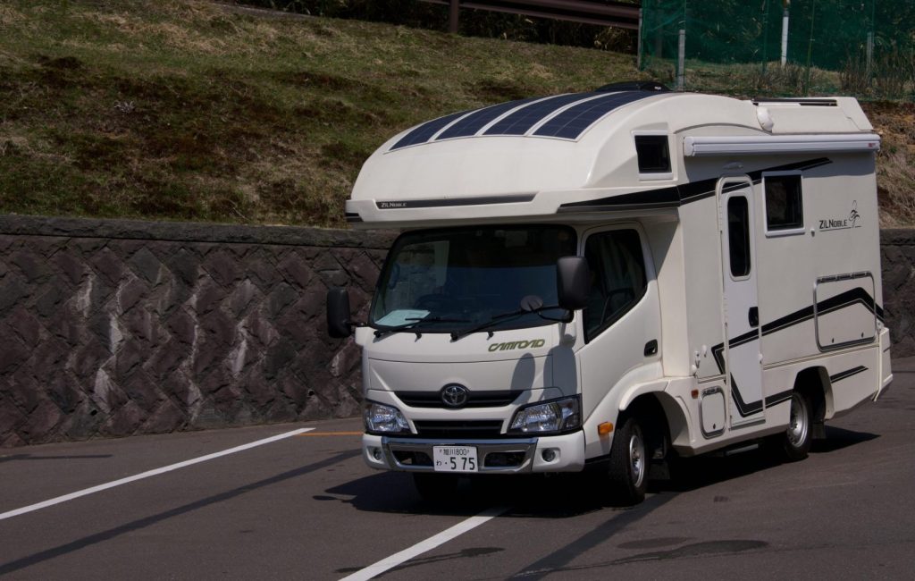 A sleek, white camper van parked on a sunny roadside, ready for adventure.
