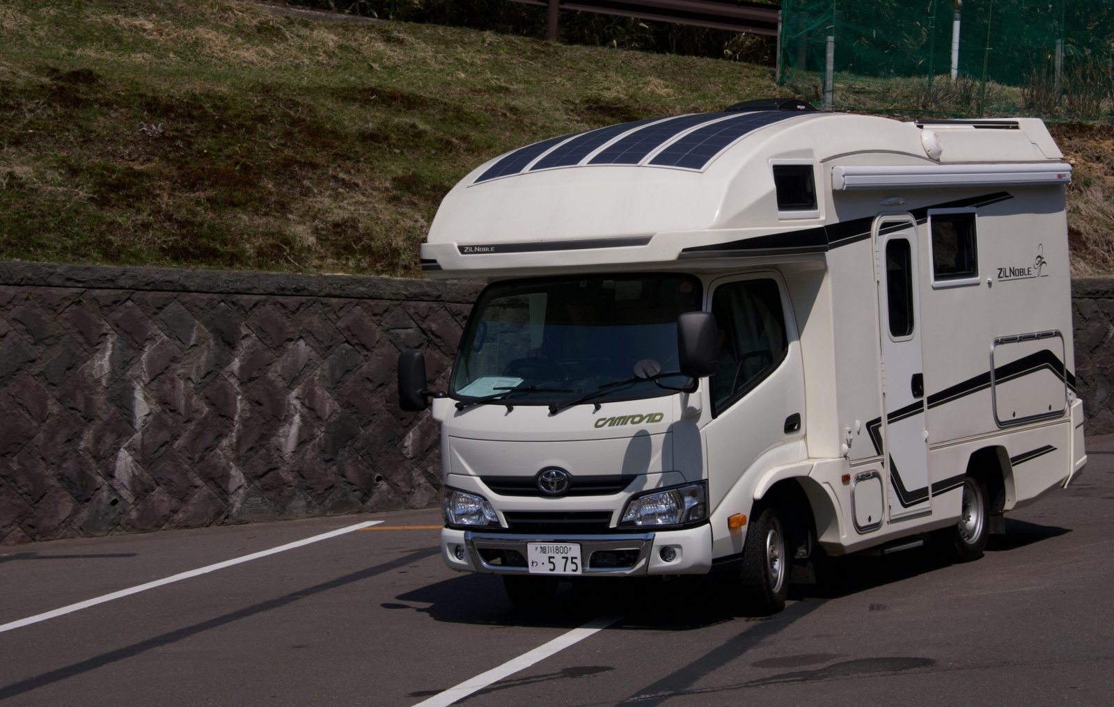 A sleek, white camper van parked on a sunny roadside, ready for adventure.